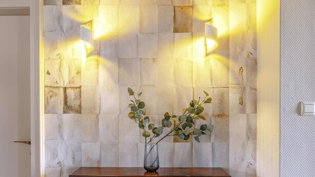 Un mur avec un motif de pierres en relief, une étagère en bois et un vase décoré de branches.