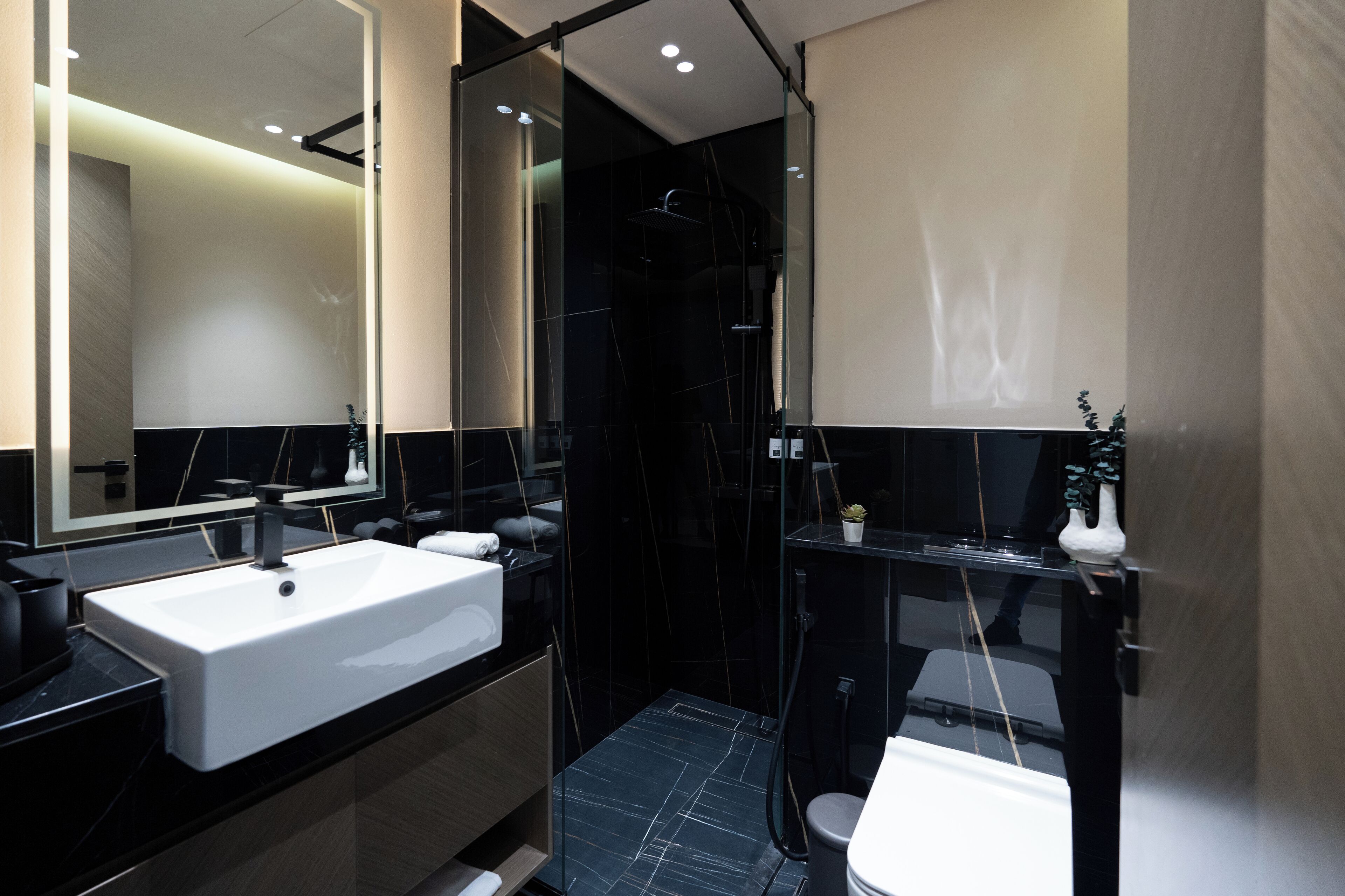 Une salle de bain moderne avec un grand miroir, un lavabo blanc, une baignoire noire et une douche séparée par une paroi de verre.