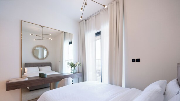 Une chambre moderne avec un grand lit, une table de chevet avec un miroir, un bureau et une fenêtre avec des rideaux.