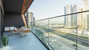 Un balcon moderne offrant une vue sur la ville, avec un coin salon doté de coussins et d’une plante en pot.