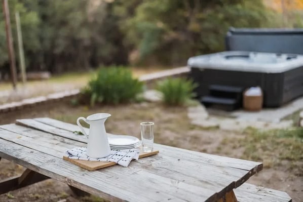 A wooden picnic table with a white pitcher, plates, and a glass set outdoors.