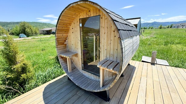 Une cabane en bois dotée d’un toit incurvé, de bancs intégrés et d’une terrasse.