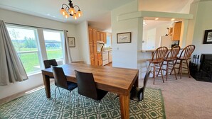Un coin repas avec une table et des chaises en bois, un tapis à motifs et une vue sur l’extérieur grâce à de grandes fenêtres.