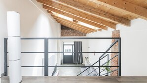 A modern interior with exposed wooden beams, a staircase, and a view to another room.