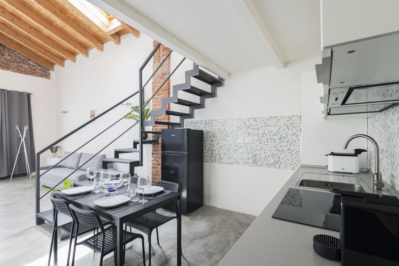 A modern kitchen with a black refrigerator, a sink, and a staircase leading to an upper level.