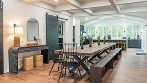 A modern kitchen with a large island, wooden flooring, and a dining area with a long table and chairs. - Luna Cove: Premier Hudson Valley Getaway (South Cairo)
