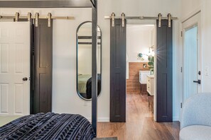 Una habitación con una cama, un tocador y un espejo. Dos puertas correderas dan acceso a otra estancia.