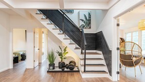 A modern staircase with a black railing, white walls, and wooden flooring. There are potted plants and decorative items on the landing. - Luna Cove: Premier Hudson Valley Getaway (South Cairo)