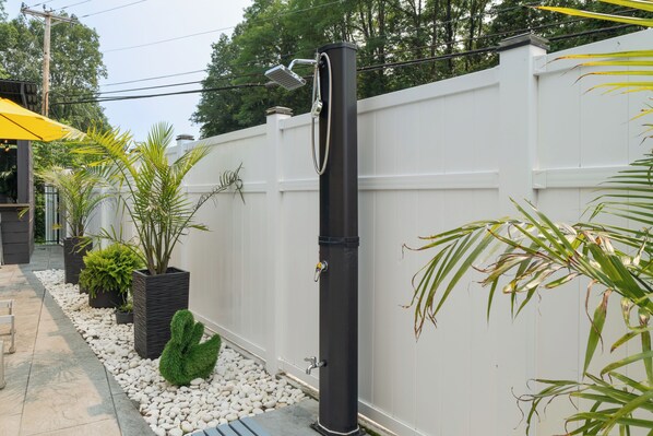 A white fence with a black post, surrounded by white pebbles and potted plants.