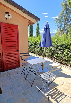 An outdoor patio with a table and chairs, a red door, and a blue umbrella.