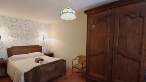 Une chambre à coucher avec un lit en bois, une armoire en bois, une chaise en osier et deux lampes fixées au mur.