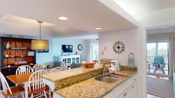 A modern kitchen with a granite countertop, white cabinetry, and a dining area with white chairs.