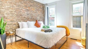 Ein modernes Schlafzimmer mit Backsteinwand, einem weißen Bett und einem großen Fenster.