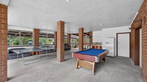 Espaço de lazer coberto com mesa de bilhar, mesa de pingue-pongue e mesa de sinuca.