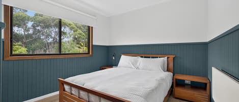 Une chambre à coucher avec un lit en bois, une table de chevet, une fenêtre donnant sur des arbres et un radiateur.