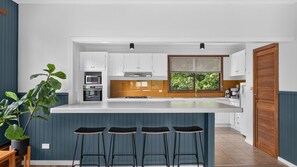 Cozinha moderna com uma ilha grande, banquetas e vista para o verde lá fora.