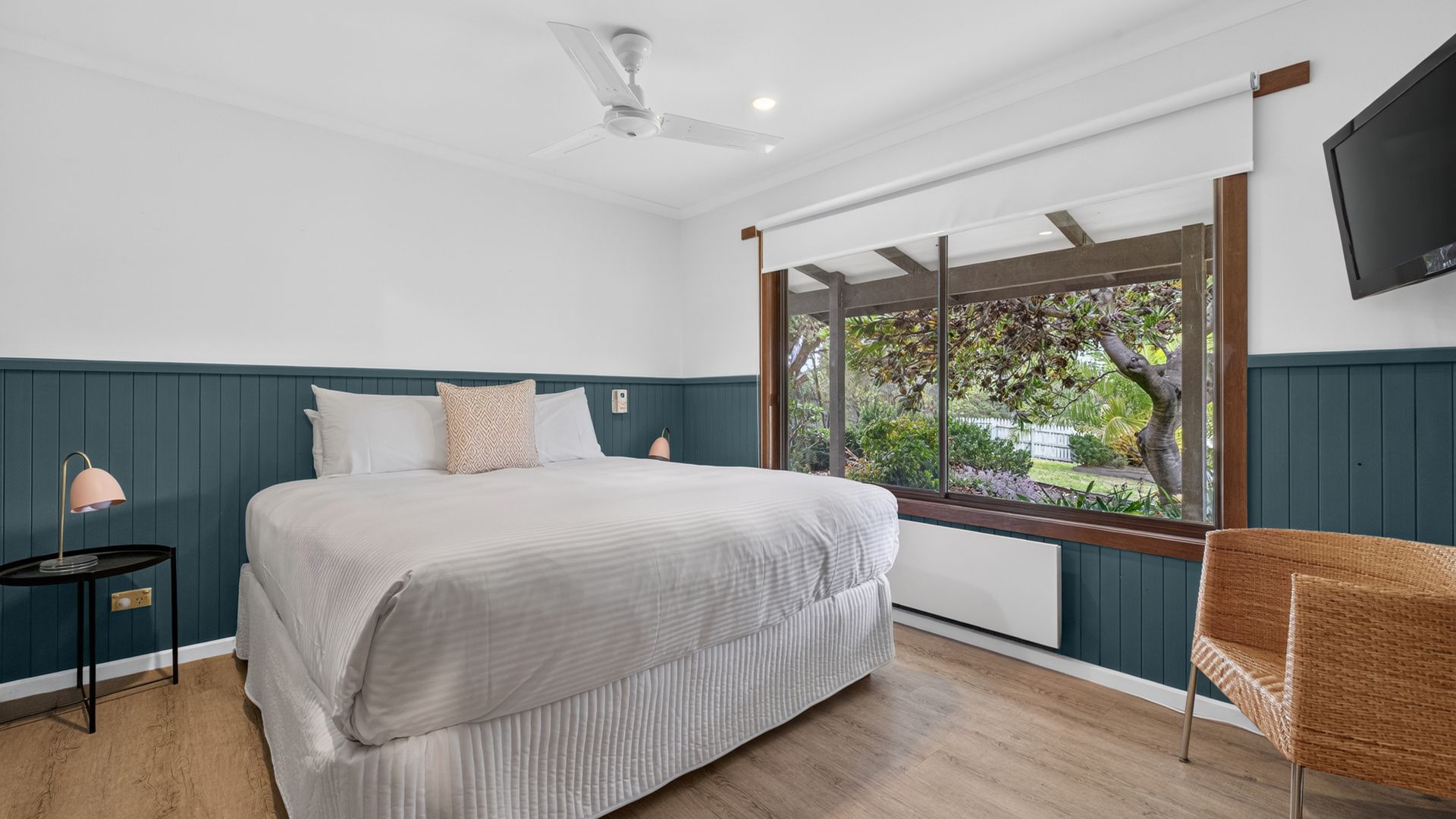 A bedroom with a bed, a nightstand, a lamp, a chair, a ceiling fan, and a TV.
