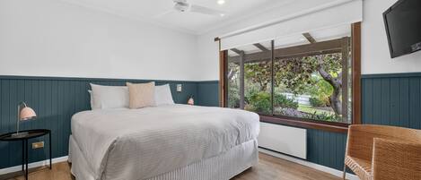 A bedroom with a bed, a nightstand, a lamp, a chair, a ceiling fan, and a TV.
