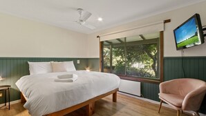 A bedroom with a bed, a chair, a TV, and a window with a view of trees.