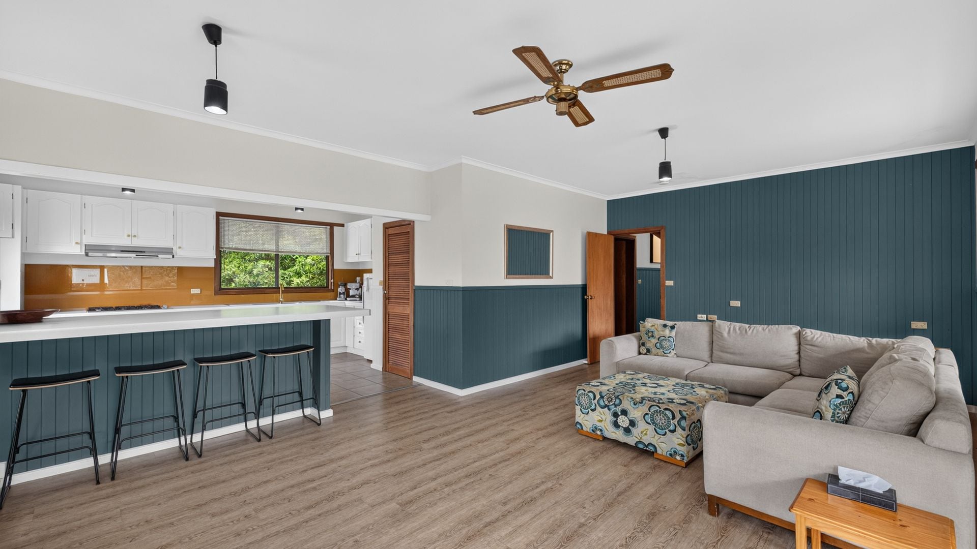A modern kitchen with a bar area, a dining table, and a sofa in a living room.