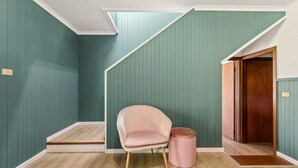 A room with teal walls, a wooden door, a pink chair, and a small round stool.