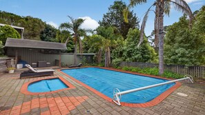 A swimming pool with a small hot tub, surrounded by a wooden deck and a fenced garden area. - Treetop Retreat House | Spacious Family Getaway (Metung)