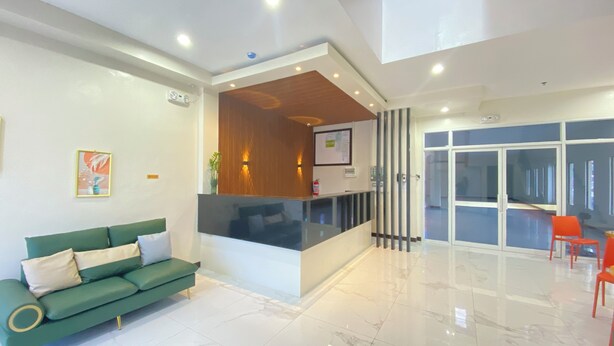 A modern hotel lobby with a green sofa, a reception desk, and a glass door leading to a dining area.