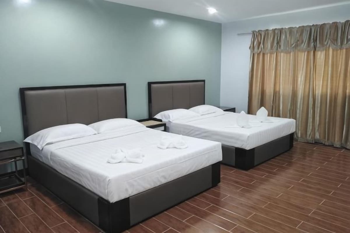 A hotel room with two beds, a nightstand, and a curtain.
