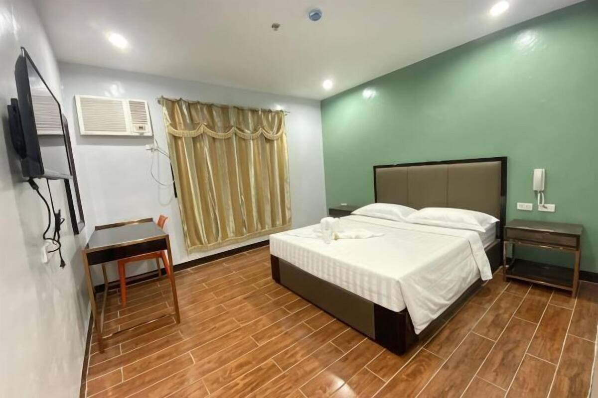 Una camera d'albergo con un letto, un comodino e una TV a muro.