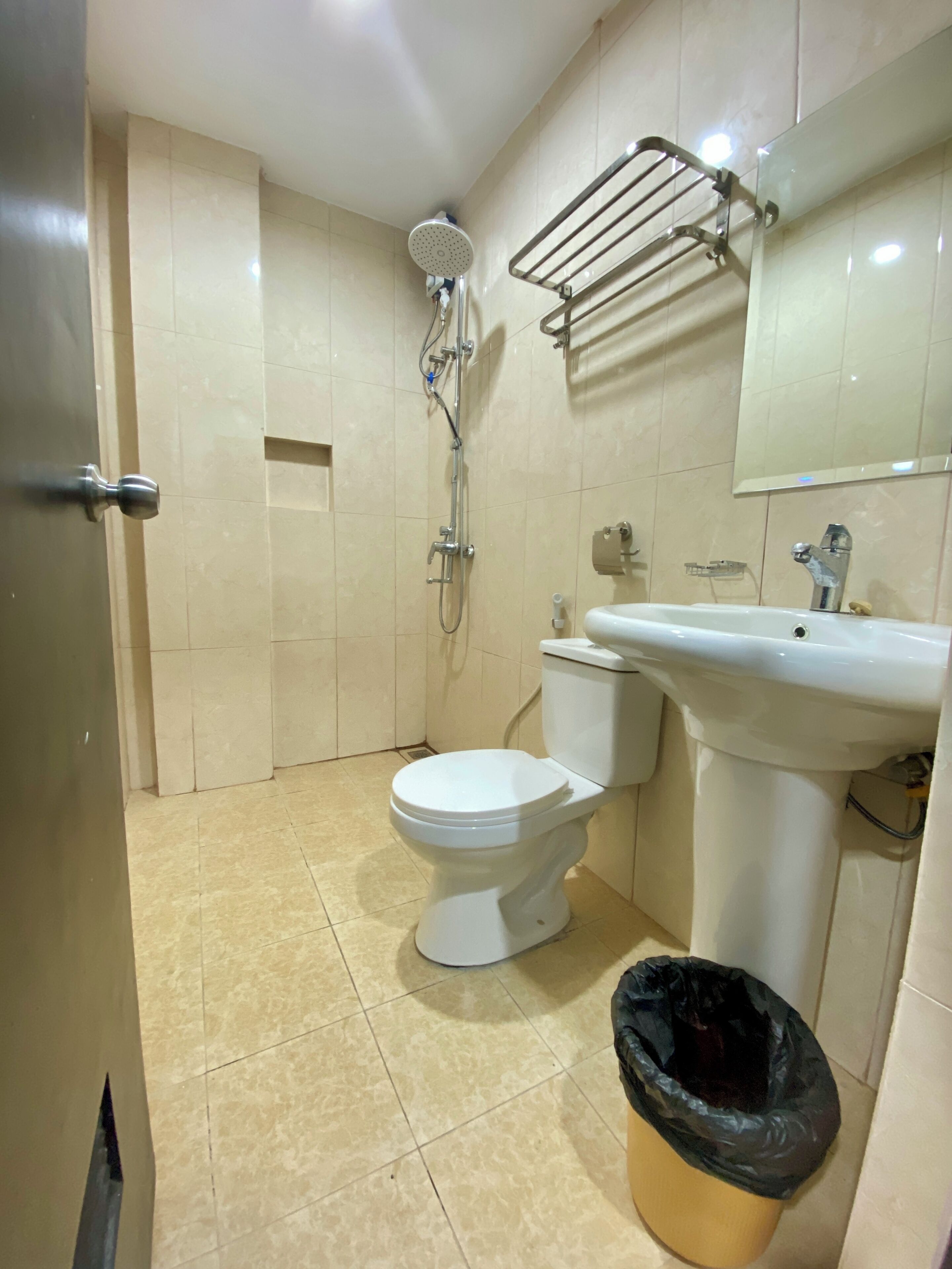 A bathroom with a toilet, sink, shower, and a trash bin.