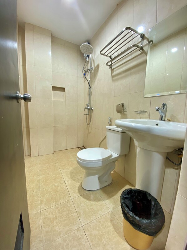 Une salle de bain équipée de toilettes, d’un lavabo, d’une douche et d’une poubelle.