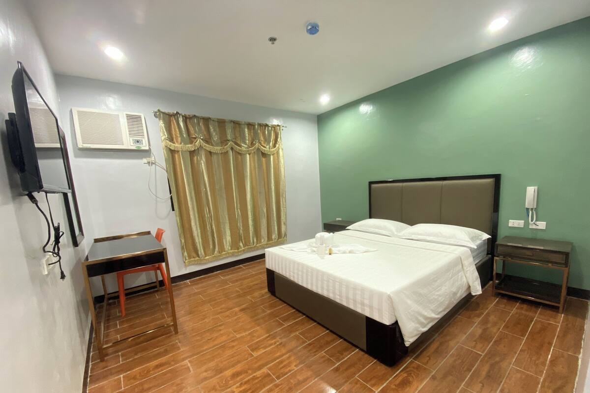 Una camera d'albergo con un letto grande, una scrivania, una sedia, una televisione, un condizionatore d'aria e un telefono.