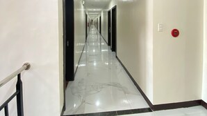A long, narrow hallway with a marble floor and black-framed doors on both sides.