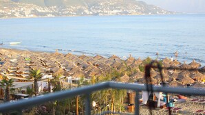 Una spiaggia con ombrelloni di paglia e lettini, vista sul mare e una cittadina in lontananza.