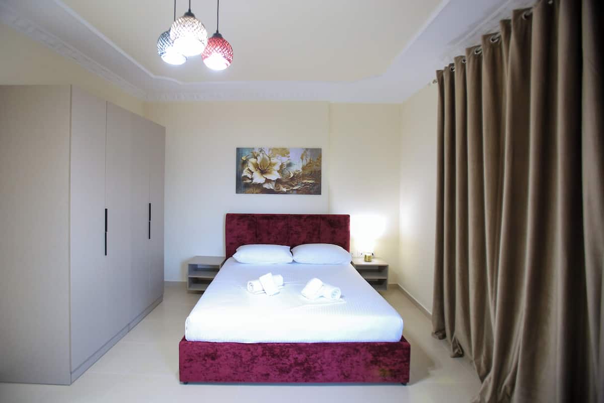 A neatly arranged bedroom with a large bed, a wardrobe, a nightstand, and a painting on the wall.