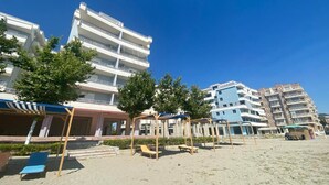 Un hotel sulla spiaggia con diversi piani, posti a sedere all'aperto e un cielo azzurro limpido.