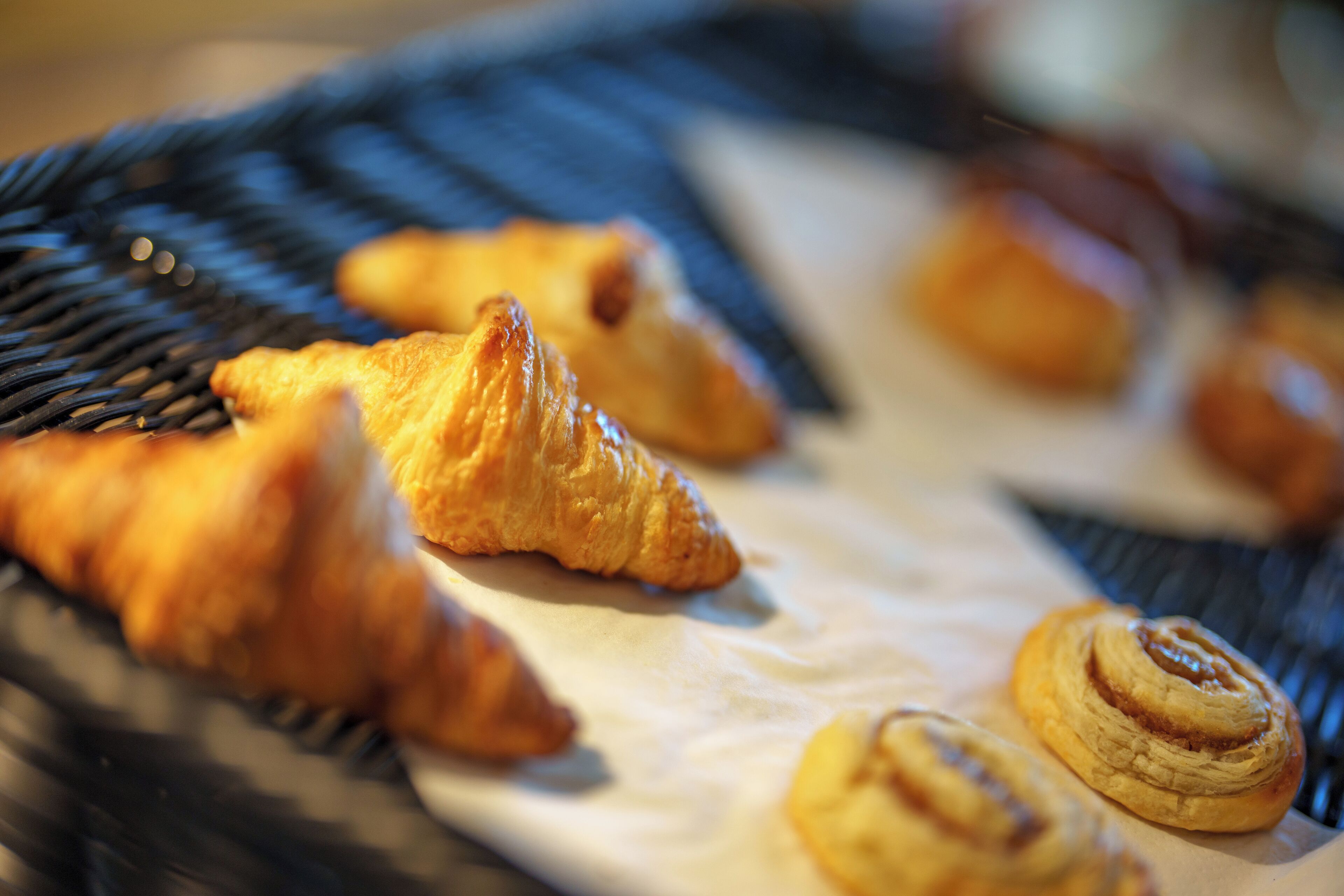 Un plateau contenant des pâtisseries, notamment des croissants et des pains aux cannelle, posé sur une surface tissée.