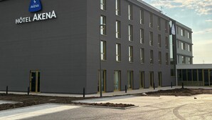 Un hôtel moderne, avec une façade sobre, de grandes fenêtres et une enseigne bien visible indiquant « HÔTEL AKENA ».
