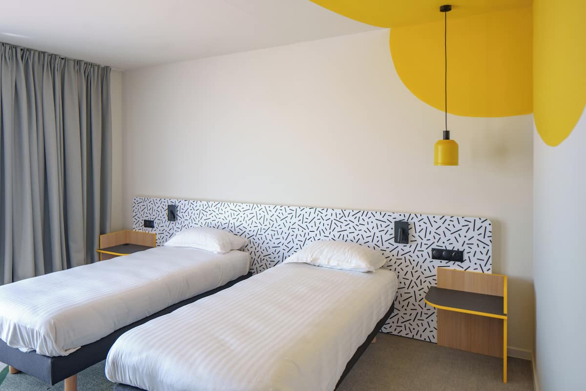 Une chambre d’hôtel avec deux lits, un bureau et une lampe suspendue jaune.