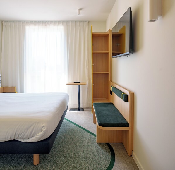A hotel room with a bed, a desk, a bench, a TV, and a wardrobe.