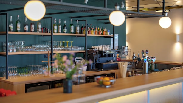 Un coin bar avec des étagères remplies de bouteilles et de verres, une machine à café et un saladier de fruits posé sur le comptoir.