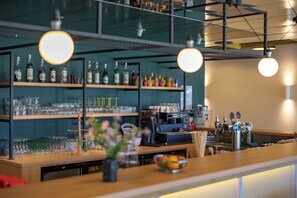 A bar area with shelves of bottles and glasses, a coffee machine, and a bowl of fruit on the counter.