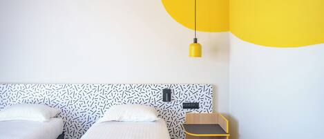 Un dormitorio moderno con dos camas, una pequeña silla de madera y un diseño de techo original.