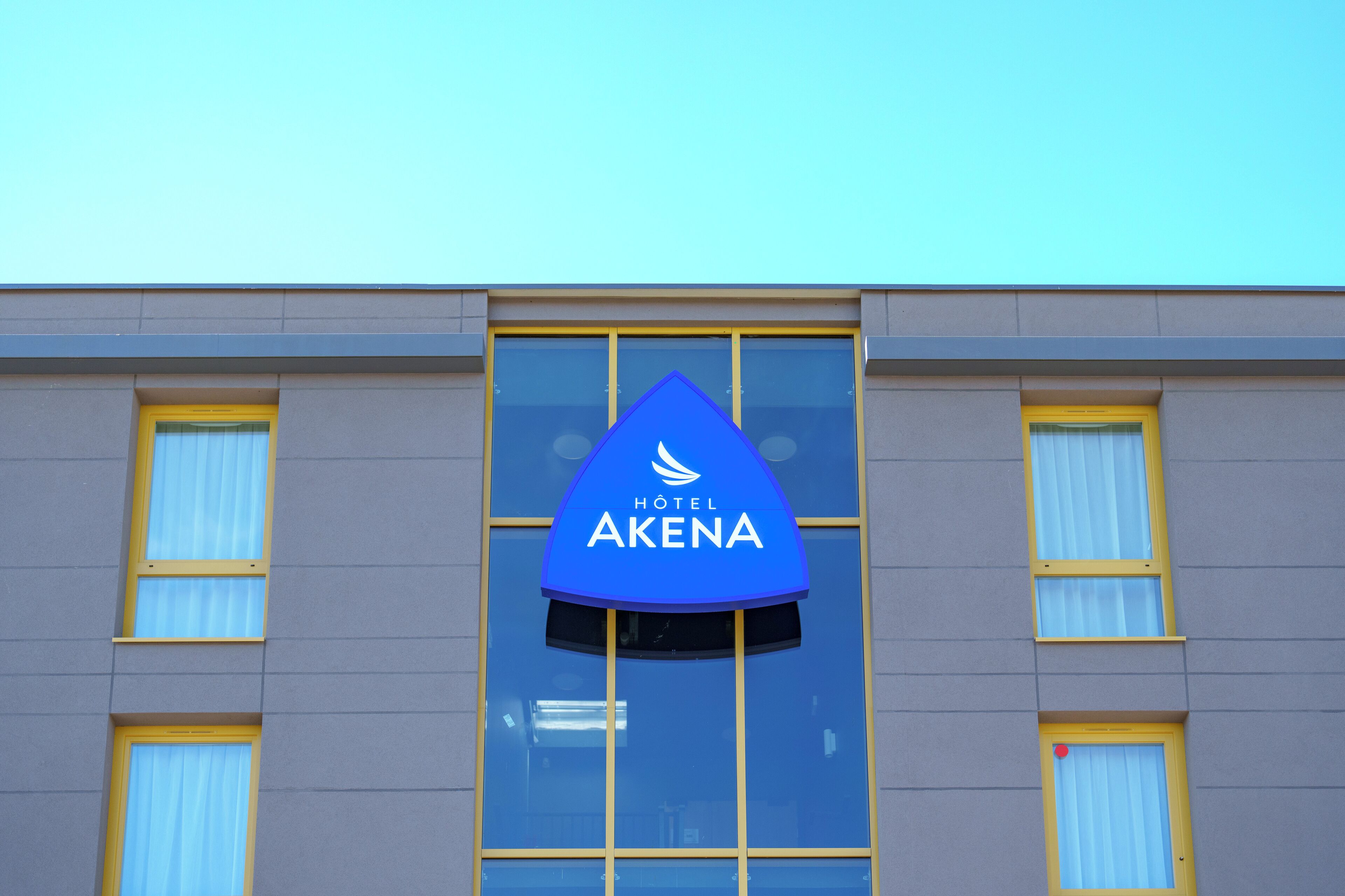 Une enseigne d'hôtel portant le nom « HOTEL AKENA » est fixée à la façade d'un immeuble.