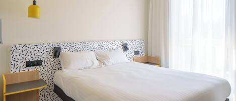 A modern hotel room with a large bed, a bedside table, a nightstand, and a hanging yellow pendant light.