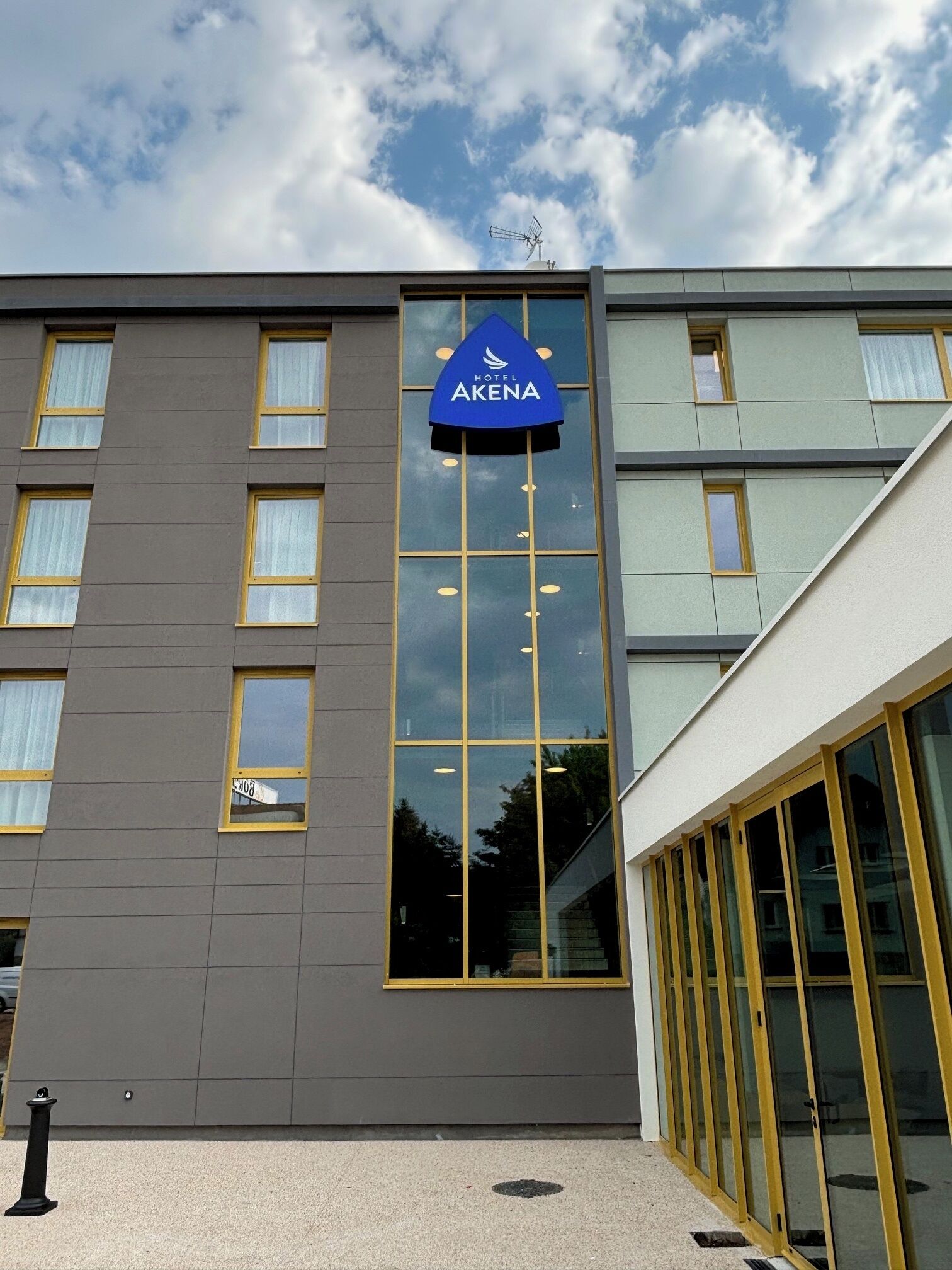 Ein modernes Hotelgebäude mit einem gut sichtbaren Schild 'Hotel Akena', großen Fenstern und einer glatten Fassade.