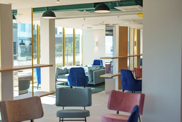 A modern interior with seating areas, large windows, and a view of the outdoors. - Hôtel AKENA HOERDT - STRASBOURG (Hoerdt)