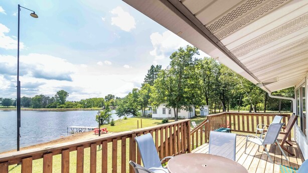 Una terraza de madera con una mesa y sillas, con vistas a un lago y una zona verde con árboles.