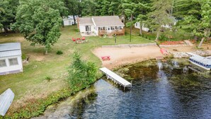 Una propiedad frente al lago con un muelle, un área de picnic techada y una casa con terraza.