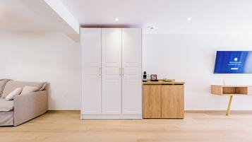Una sala de estar moderna con un sofá color beige, un armario blanco, un mueble de madera y un televisor montado.